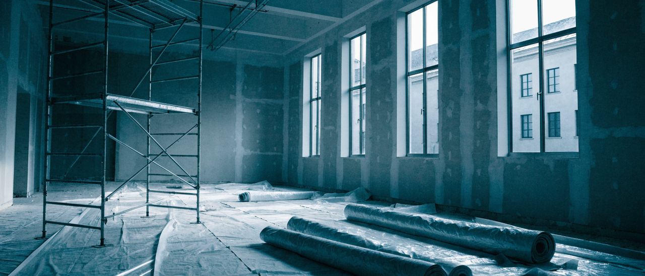 Open commercial interior with suspended work lighting and protective floor covering during ceiling work