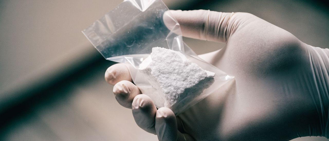 Gloved hand collecting a small sample of ceiling texture into a labeled specimen bag