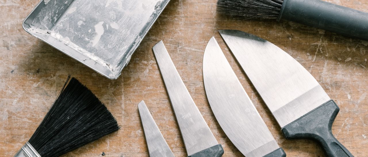 Drywall taping knives, mud pan, and sanding pole laid out on a work surface